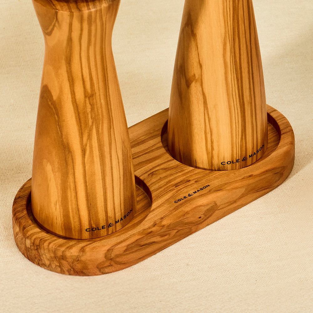 The Cole & Mason Portobello Olive Wood Mill Tray features rounded edges and two circular indentations, making it a stylish salt and pepper mill tray or elegant kitchen organizer. Its smooth, natural grain looks great on any countertop.