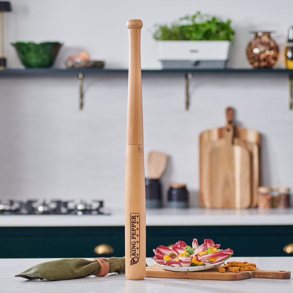 A 710mm King Pepper Baseball Bat Pepper Mill by Cole & Mason UK stands upright on an off-white background, its light natural finish features a Tiny Peppy logo near the bottom and a design inspired by the classic King Pepper mill.