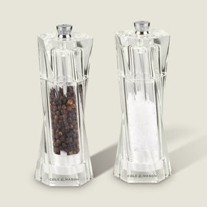 The Cole & Mason Aldeburgh Salt & Pepper Mill Set features two clear acrylic mills with adjustable grinding, filled with black peppercorns and coarse sea salt, standing side by side on a light background.
