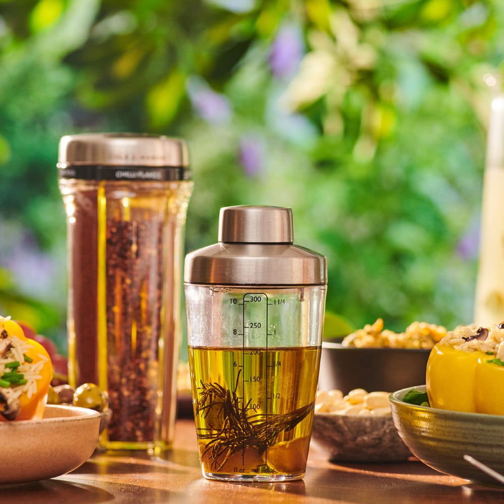 The Cole & Mason Cambourne Salad Dressing Shaker features clear glass with a stainless steel lid and measurement lines in ounces, milliliters, and cups—ideal for mixing cocktails, vinaigrettes, or dressings on any surface.
