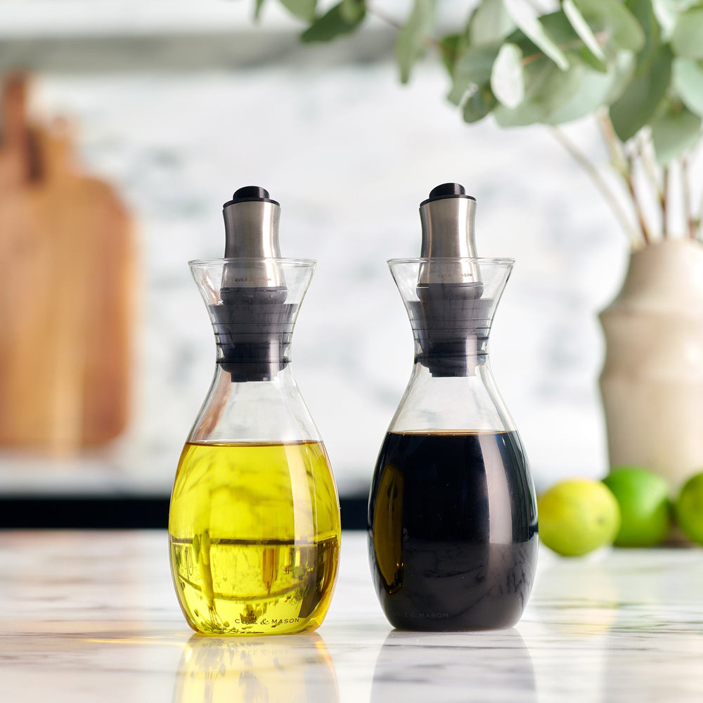 The Cole & Mason Haverhill Oil & Vinegar Pourer, filled with golden yellow oil, has a silver and black precision pour spout for drip-free use and is displayed against a light gray background.