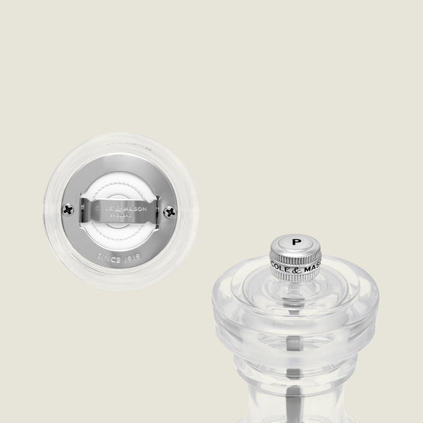 The Cole & Mason Acrylic Salt Shaker & Pepper Mill Set, 104 mm, is showcased in close-up against an off-white background to emphasize its clear acrylic body, adjustable grinding mechanism, metallic accents, engraved branding, and top cap.