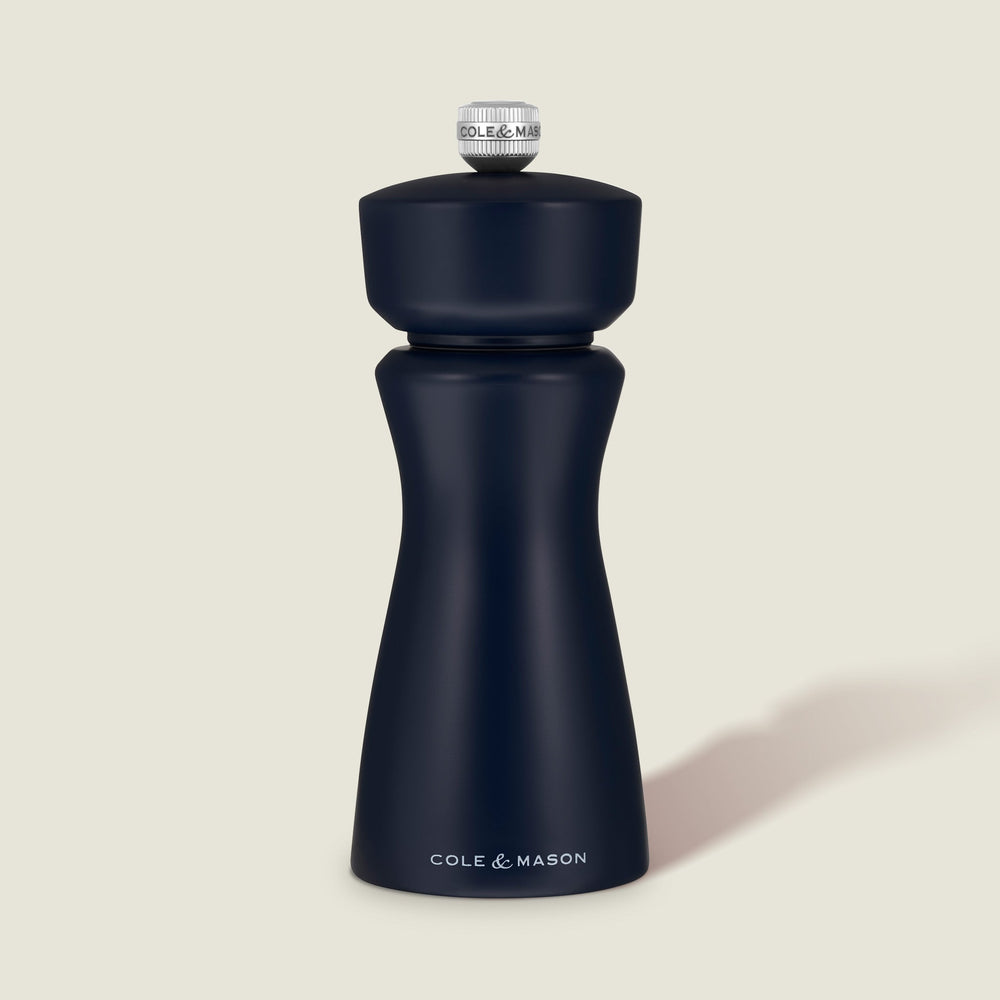A Persian Blue Cole & Mason Kenton Salt & Pepper Mill, featuring a high-quality ceramic grinder and a sleek design, stands upright on a light beige background, casting a soft shadow to the right.