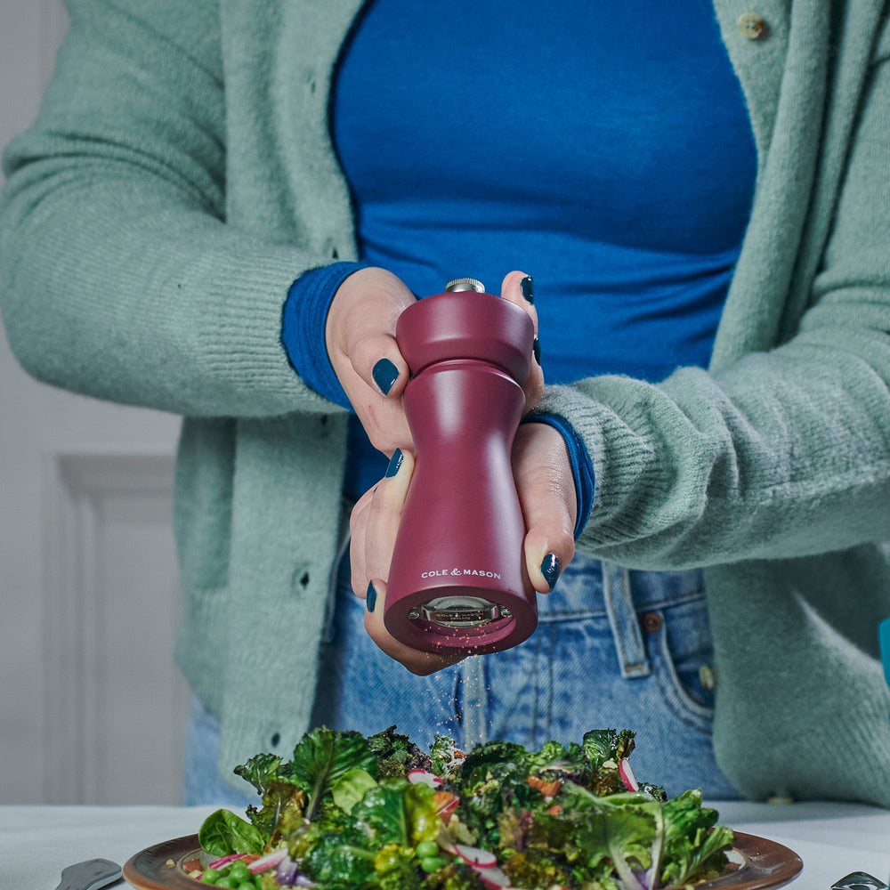 The Cole & Mason Kenton Sichuan Pepper Red Salt & Pepper Mill, with a matte burgundy finish, ceramic mechanism, and silver top knob, stands upright on a plain light background with the brand logo in white near its base.