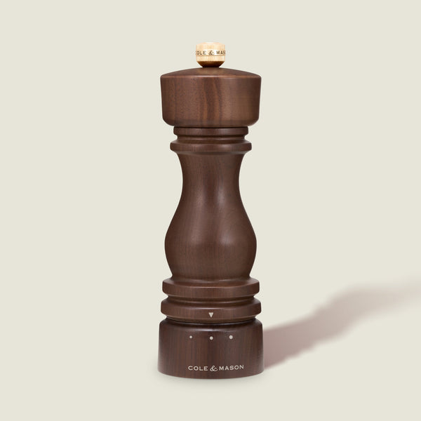 A London Walnut Salt or Pepper Mill from Cole & Mason, featuring dark walnut wood with a rounded top and base, stands upright on a light beige background.